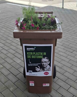 Mit Blumen bepflanzte Biotonne mit dem Hinweis: Kein Plastik in die Biotonne